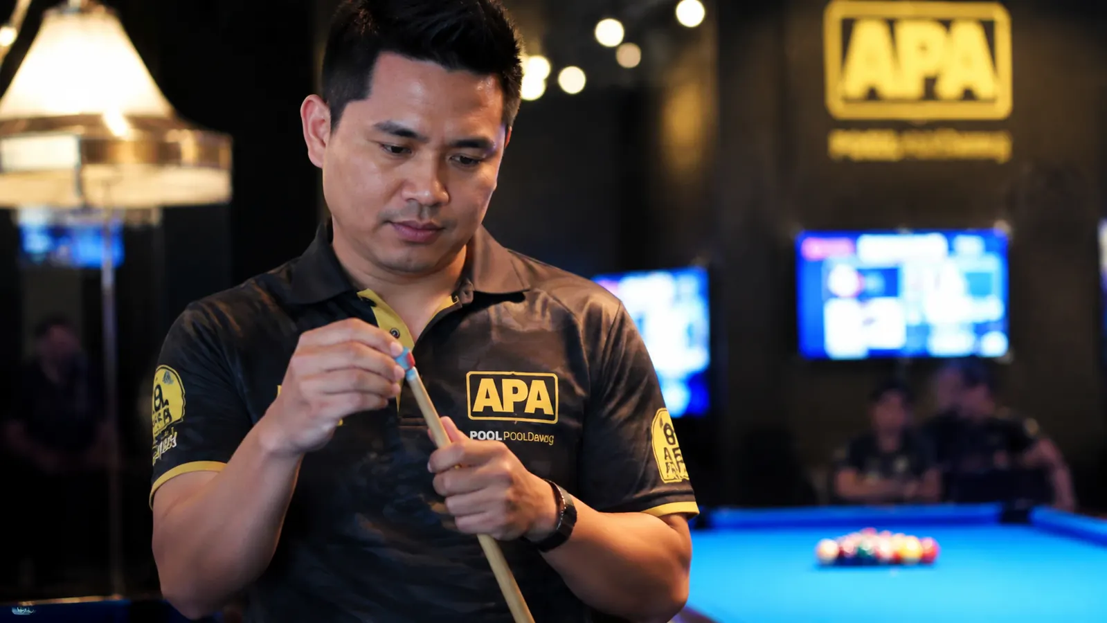 A pool player in a league jersey setting up for the break shot with a dedicated break cue