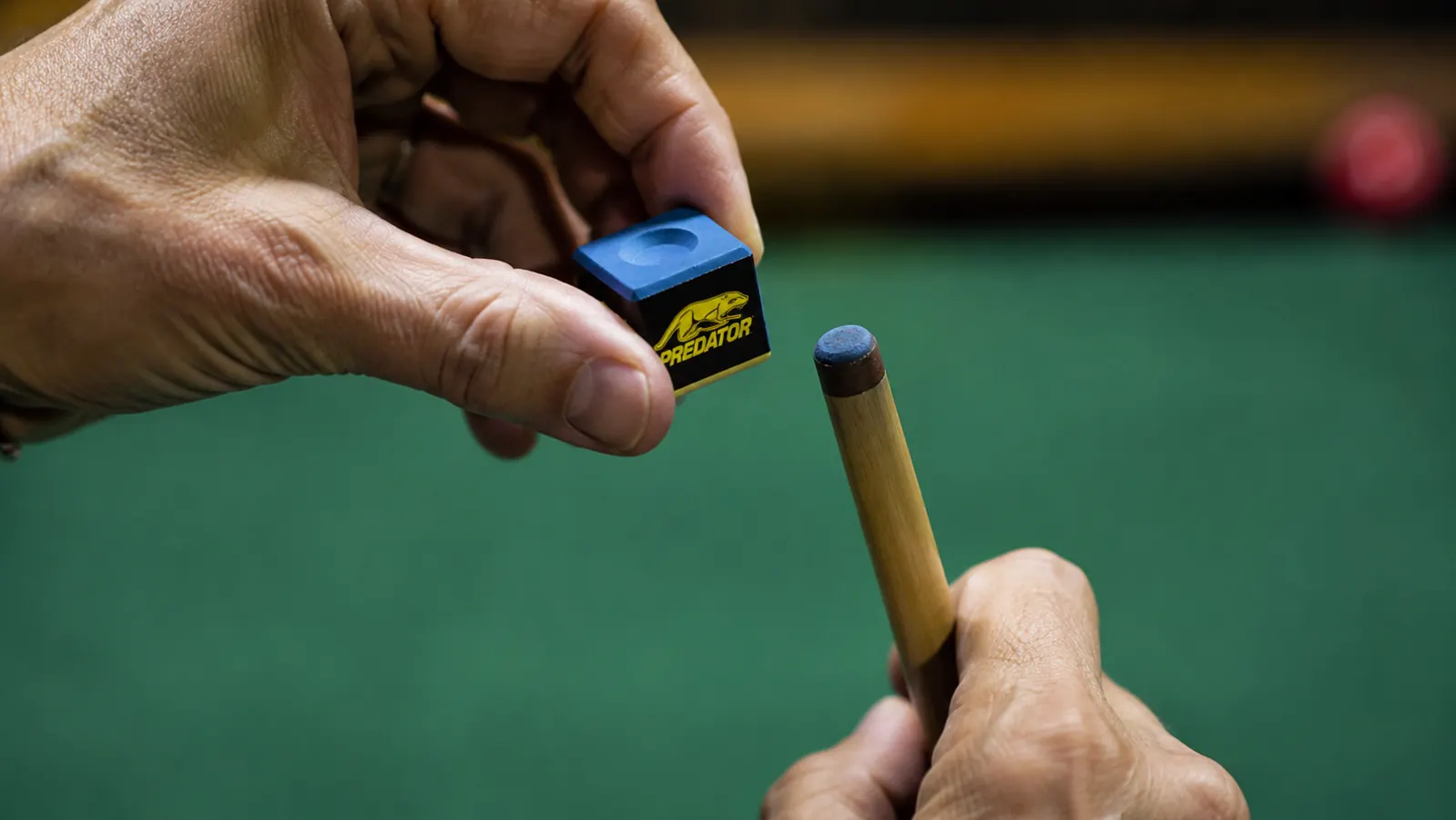 Hand holding a cube of Predator chalk against a green felt pool table background