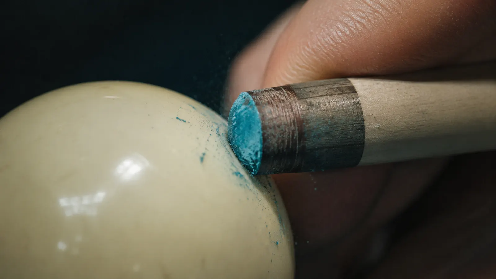 Close-up of a pool cue tip making contact with the cue ball showing chalked tip impression