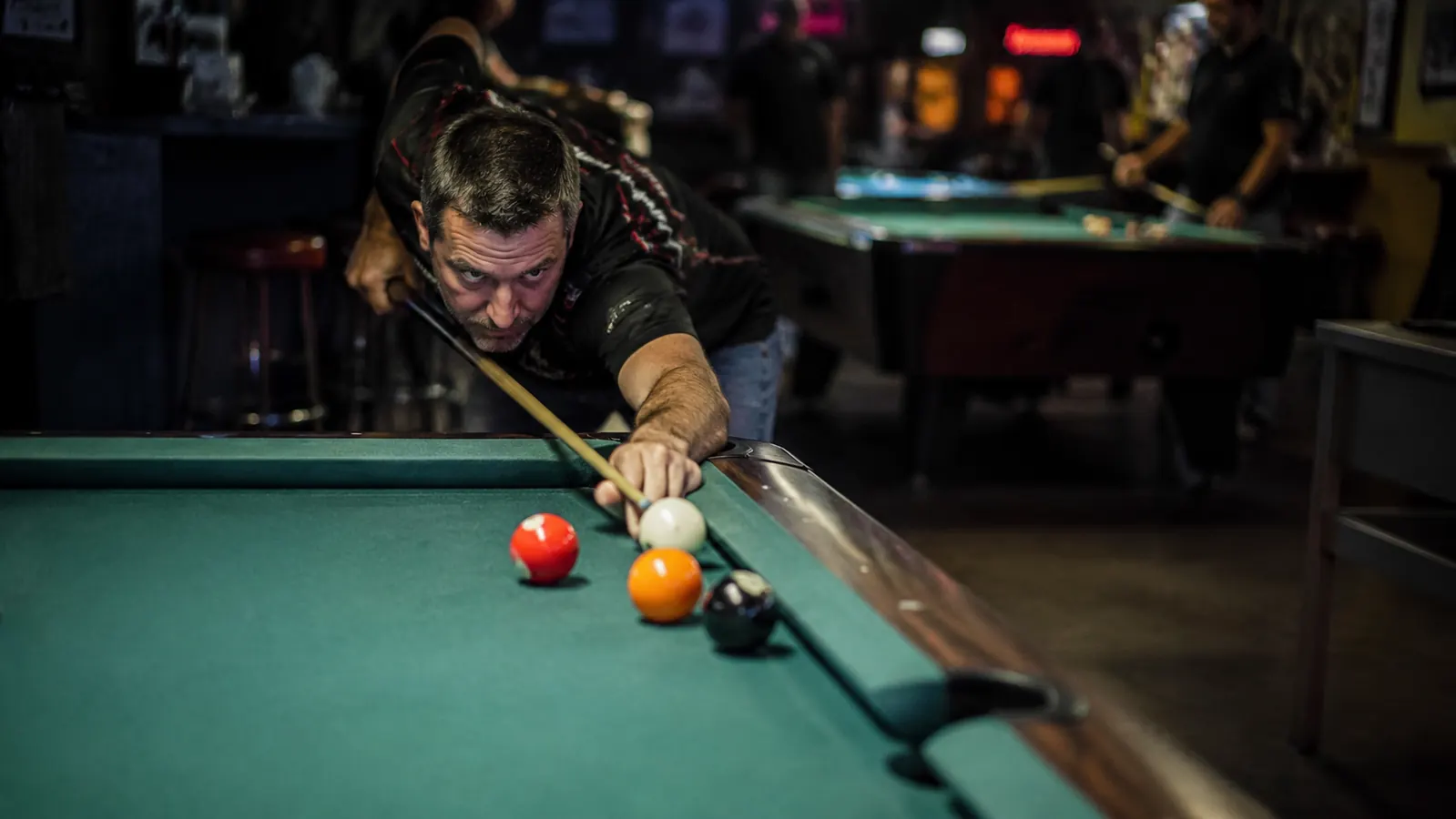 Player lining up a sharp cut shot in a bar league setting with overhead lighting