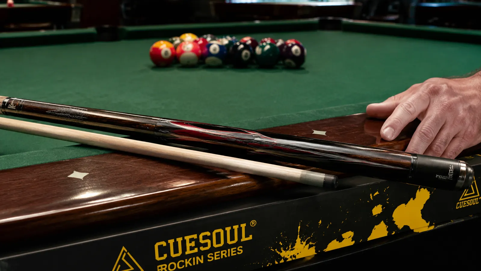 CUESOUL Rockin Series pool cue laid across a pool table rail next to a set of billiard balls