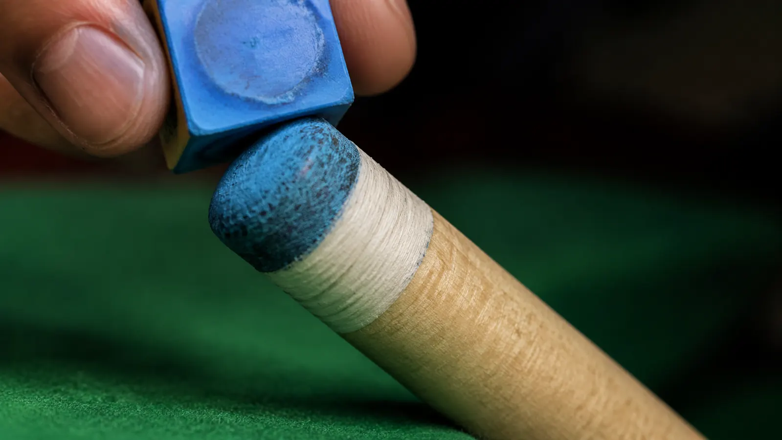 Close-up of a pool cue tip being chalked with a small blue cube of chalk