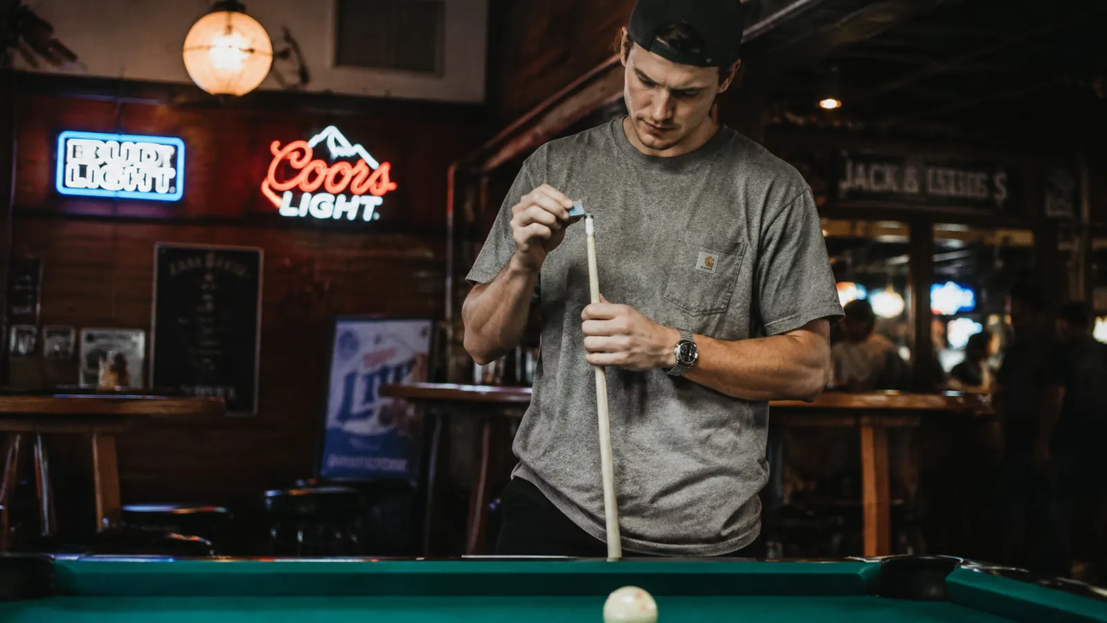 A pool player chalking a cue at a bar pool table under neon lighting