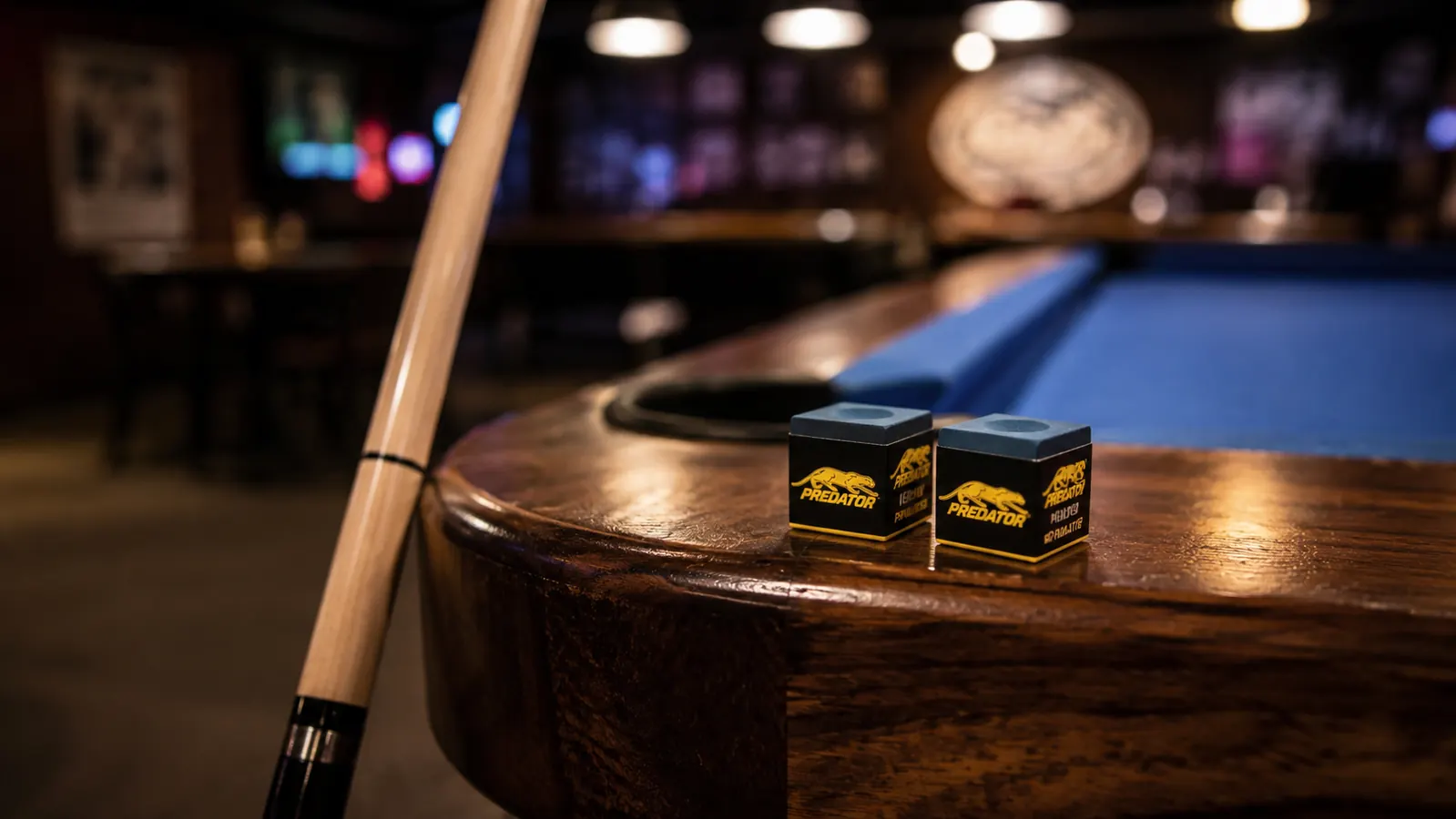 Predator chalk cubes lined up on the rail of a pool table next to a cue stick
