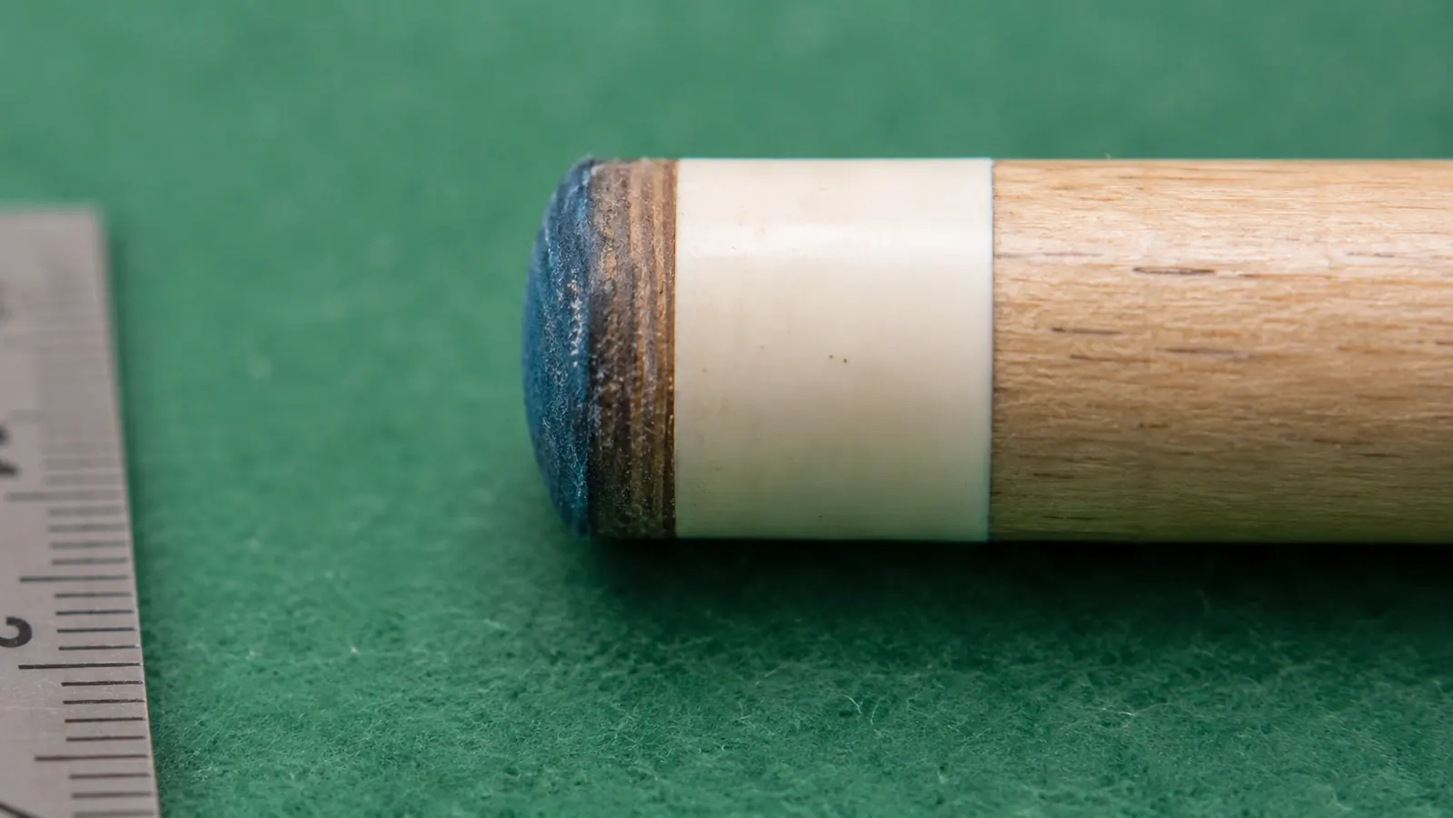 Pool cue tip up close showing tip diameter measurement with a coin for scale