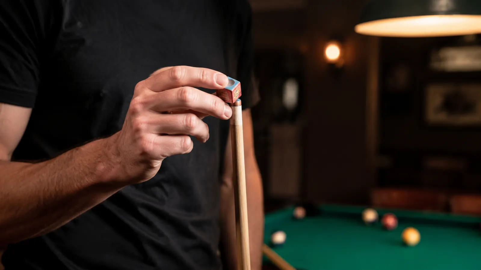 Player chalking a pool cue at a billiards table preparing for a shot