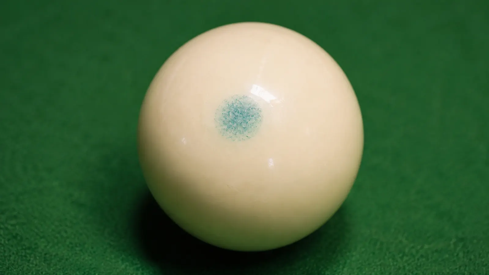 Teal chalk dust residue on a white cue ball after a heavy draw shot at a league match