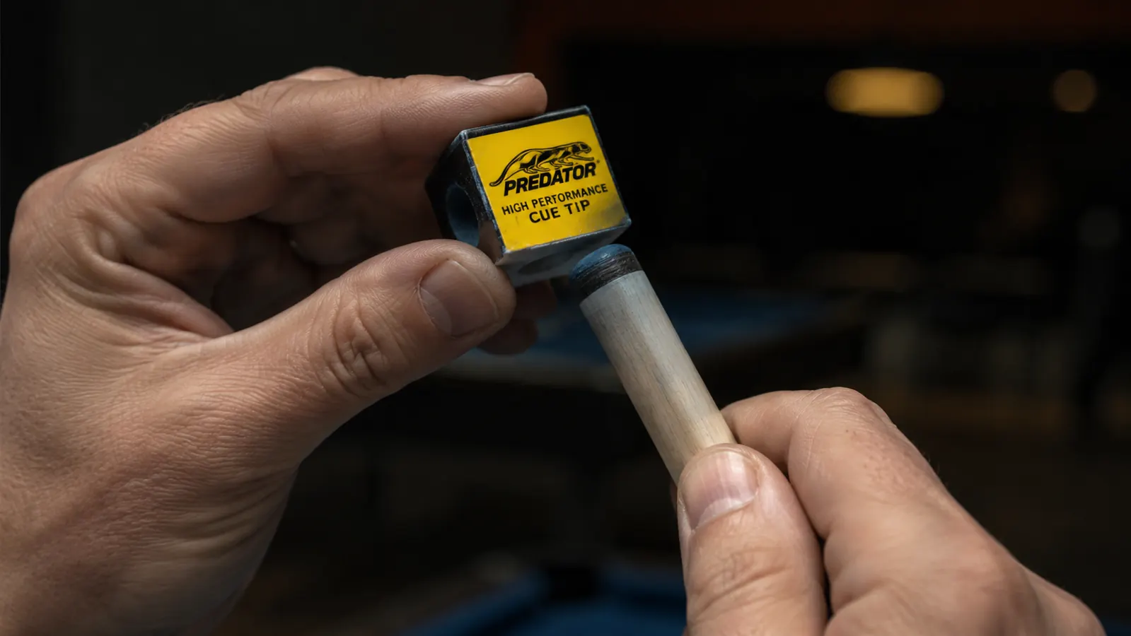 Close-up of a hand applying Predator chalk to the leather tip of a pool cue, dark background