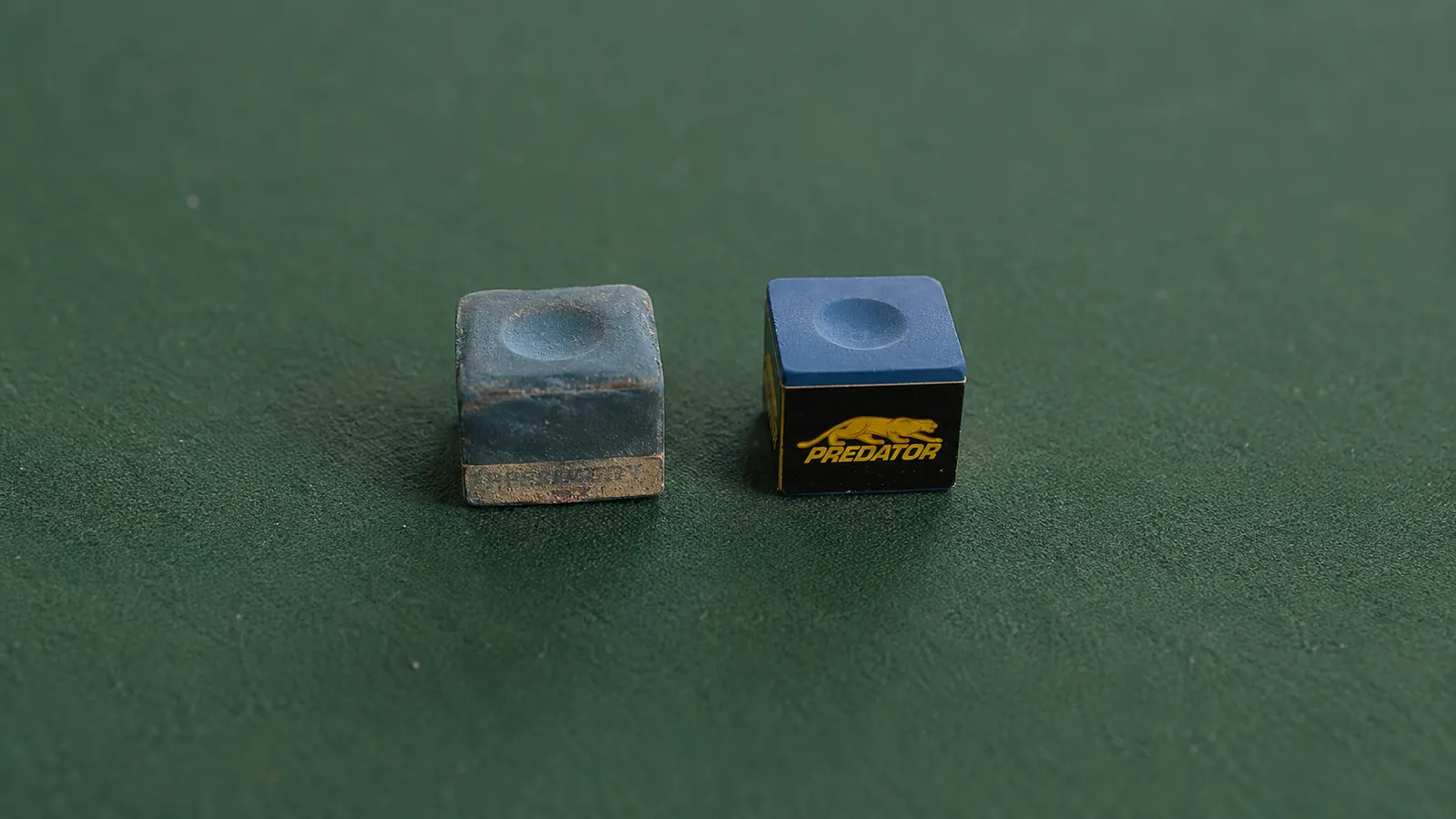 Two chalk cubes side by side on green felt -- one worn-down generic cube, one Predator blue cube