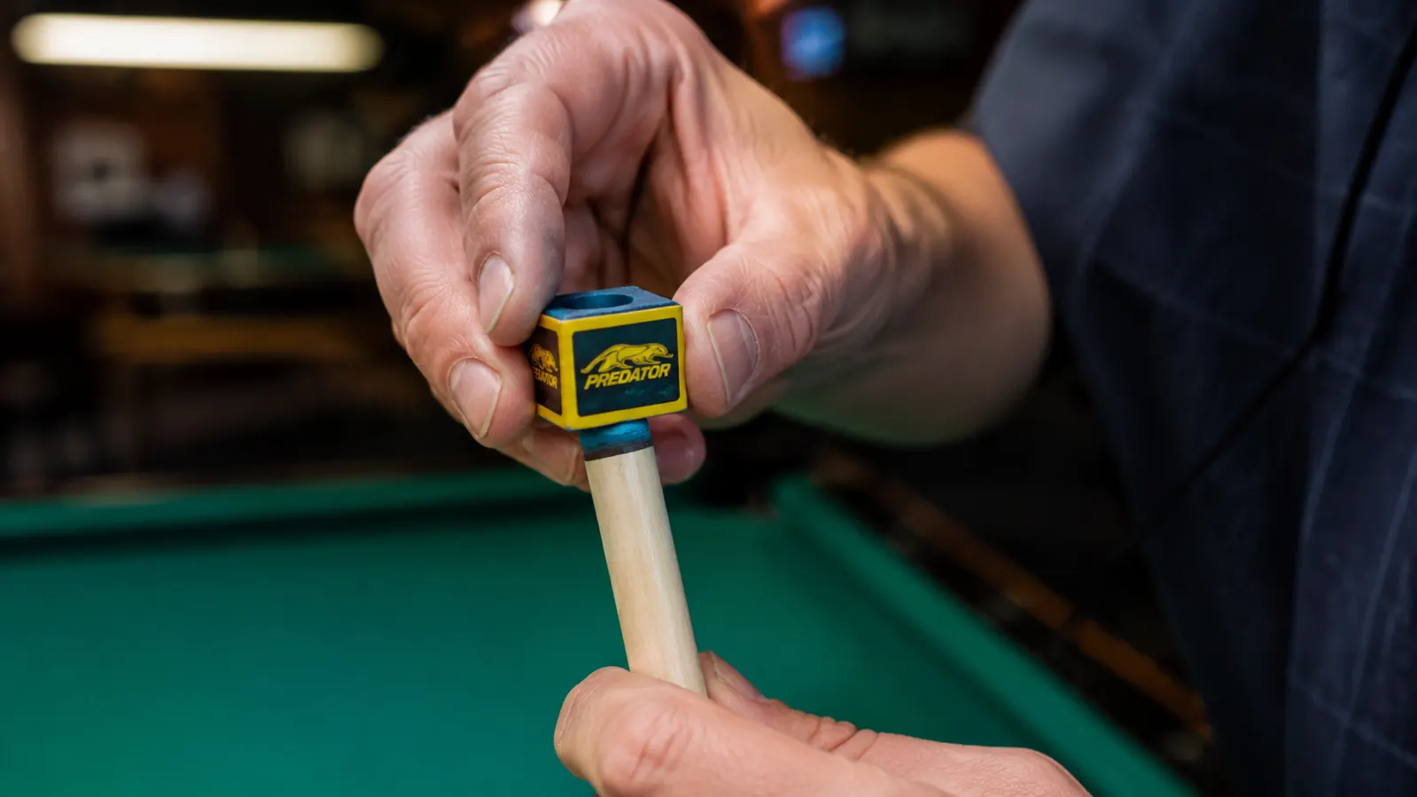 Hand chalking a pool cue tip with a cube of Predator chalk before a shot
