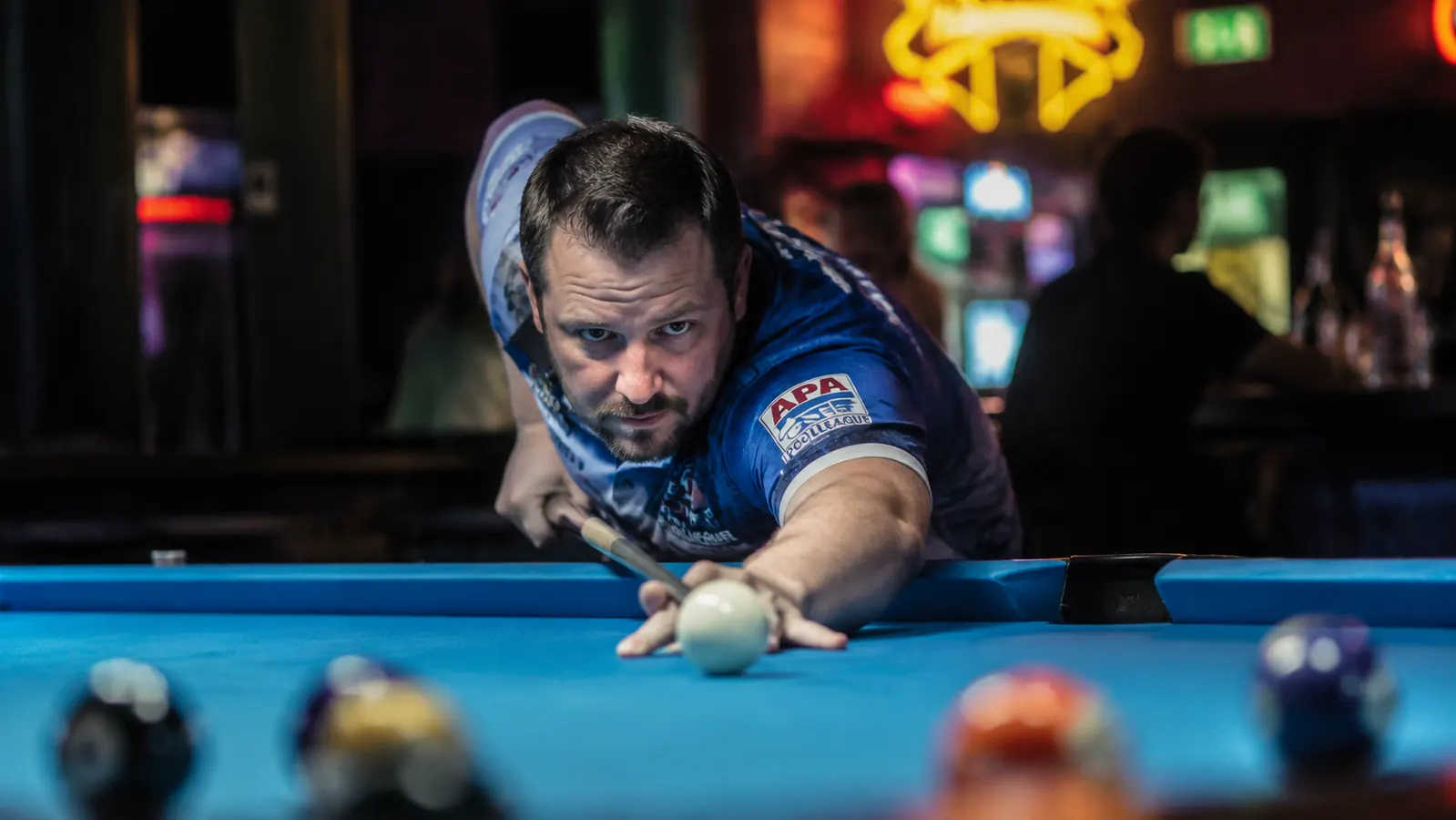 Pool player in league shirt gripping a break cue at the bridge position, ready to execute a powerful break shot
