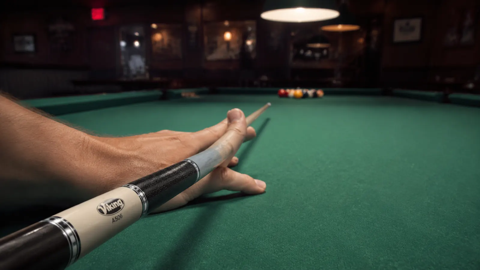Pool player's bridge hand on green felt, cue shaft resting in open bridge, shot lined up at far end of table