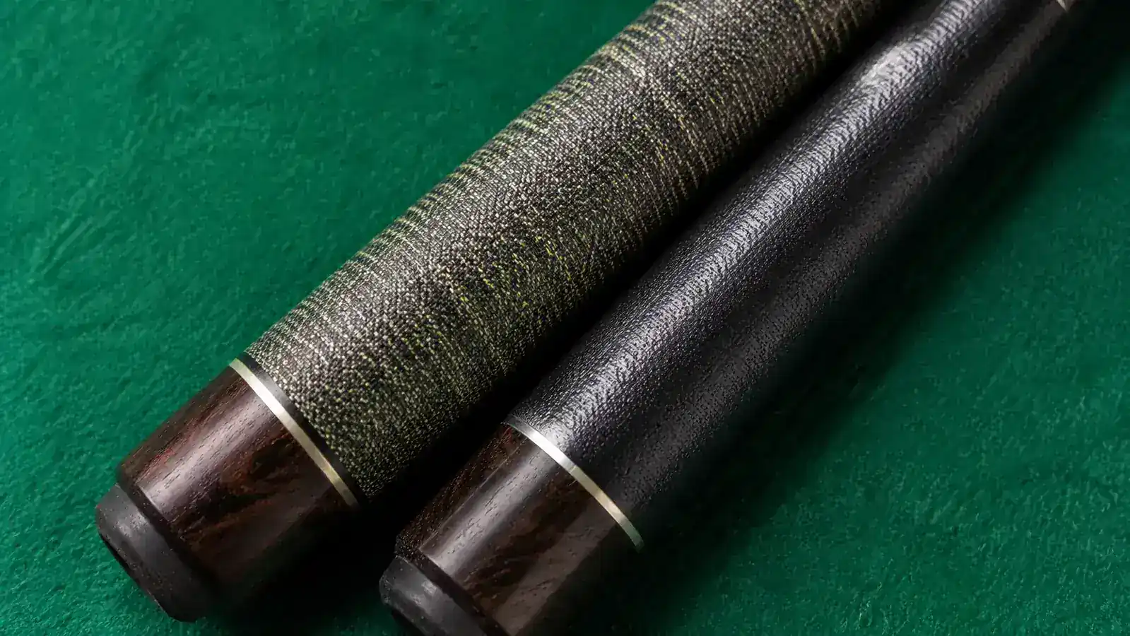 Two pool cues side by side on a billiards table showing wrap texture difference between linen and synthetic
