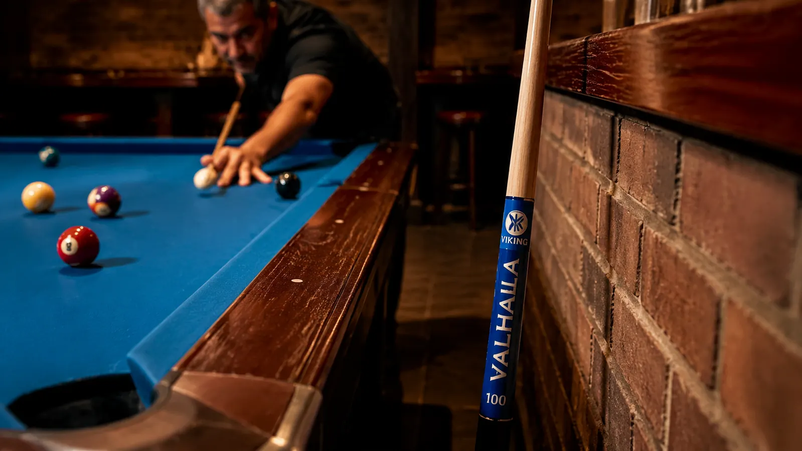 The Viking Valhalla 100 Series pool cue standing upright against a brick wall in a pool hall