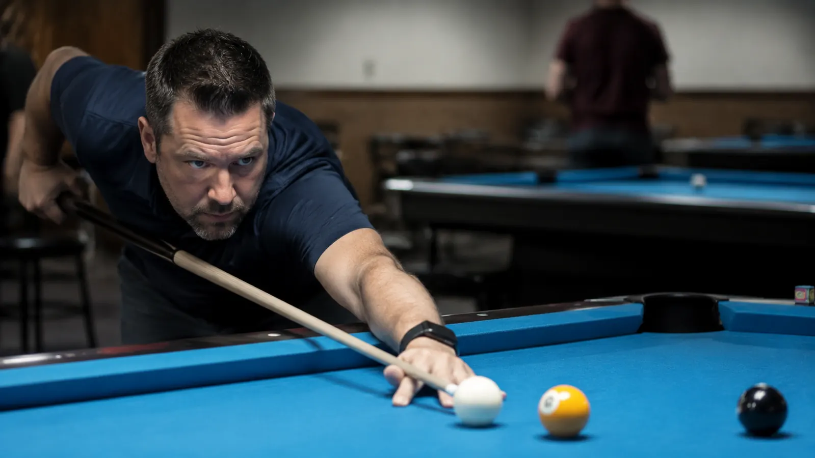 Pool player lining up a spin shot in a dimly lit league hall, cue extended across table